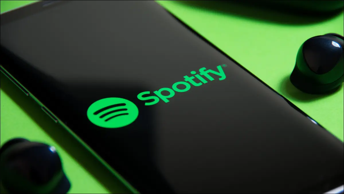 緑の背景にワイヤレスイヤフォンの横にSpotifyのロゴを表示しているスマートフォン。