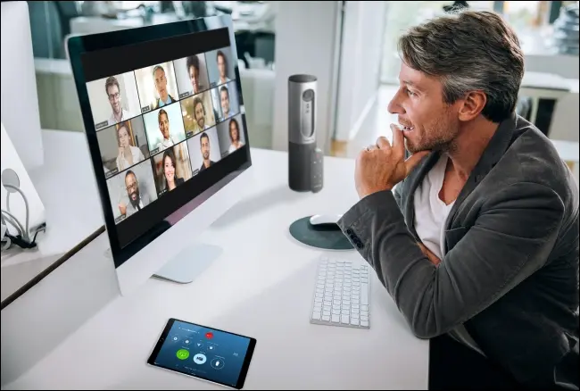 Un uomo durante una riunione Zoom sul suo Mac con i partecipanti in Visualizzazione galleria sul monitor.