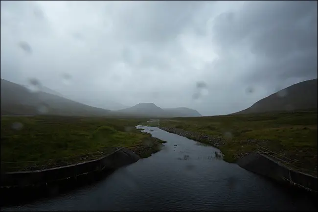 一张山和溪流的雨天照片，镜头上有水滴。