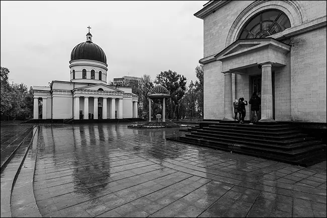 Die Spiegelung eines Gebäudes auf einem nassen Backsteinhof in einem Schwarz-Weiß-Foto.