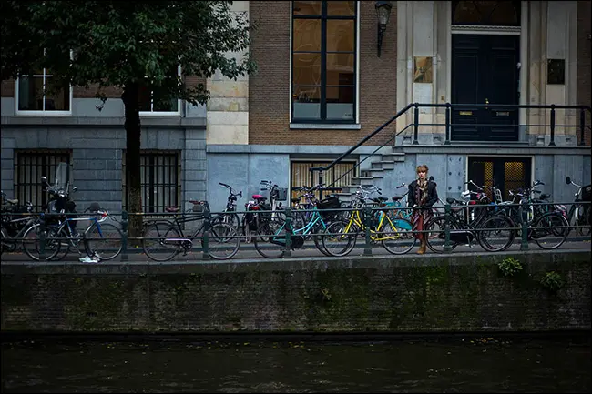 Une femme debout sur un pont derrière une ligne de vélos garés.