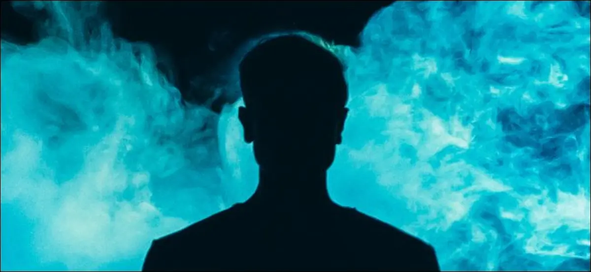 Una silhouette di un individuo davanti al fumo blu su uno sfondo scuro.