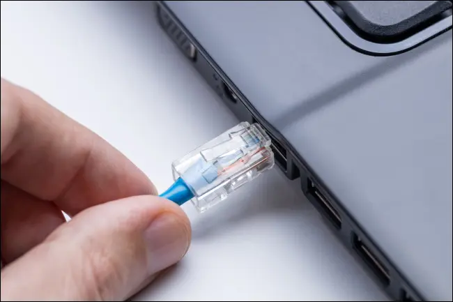 Uma mão conectando um cabo Ethernet em um laptop.