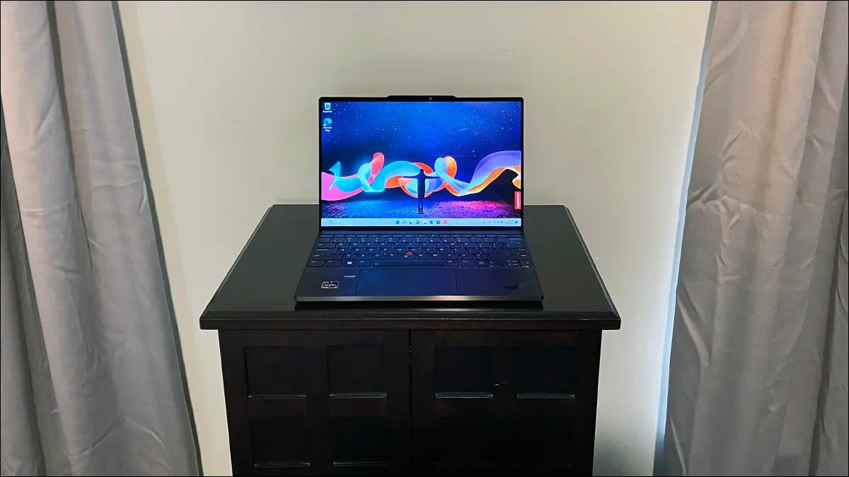 Un portátil con pantalla táctil Lenovo ThinkPad Z13 Gen 1 abierto sobre una mesa entre dos cortinas