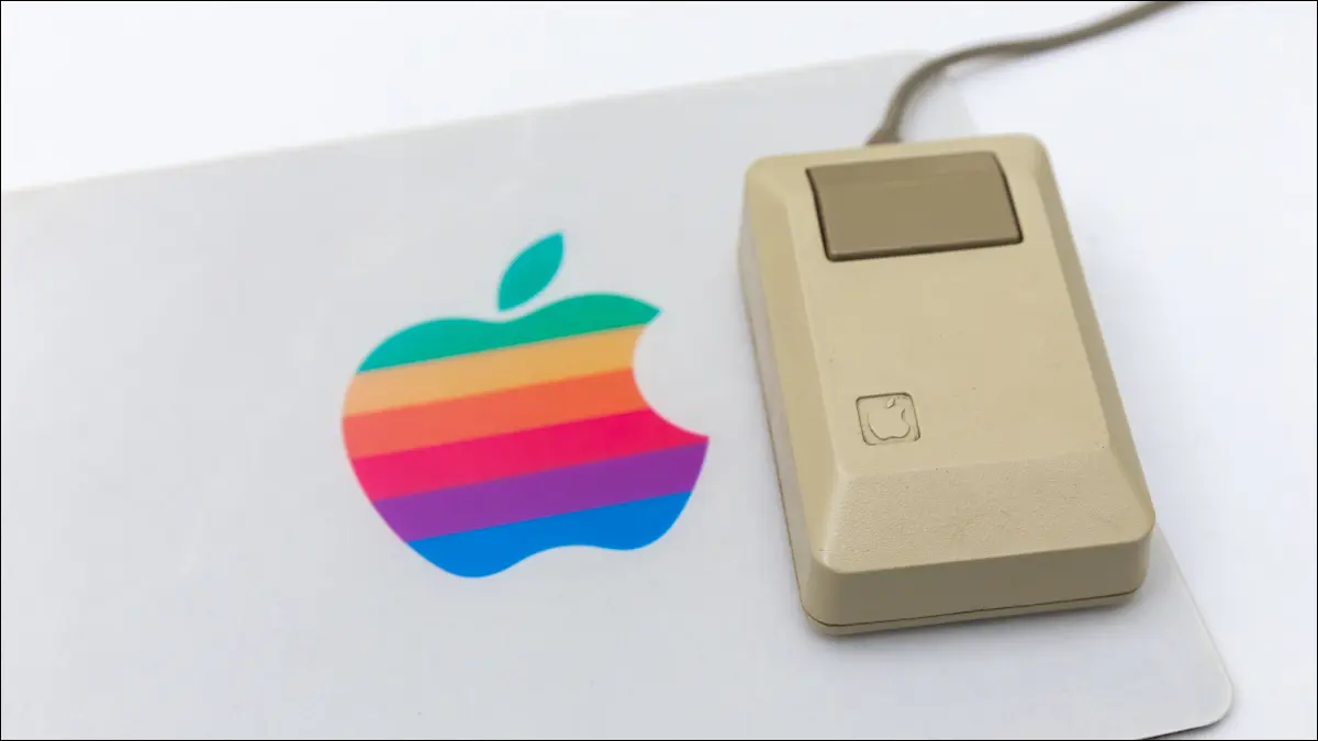 Un mouse de computer Apple de epocă pe un mousepad cu logo-ul Apple curcubeu.