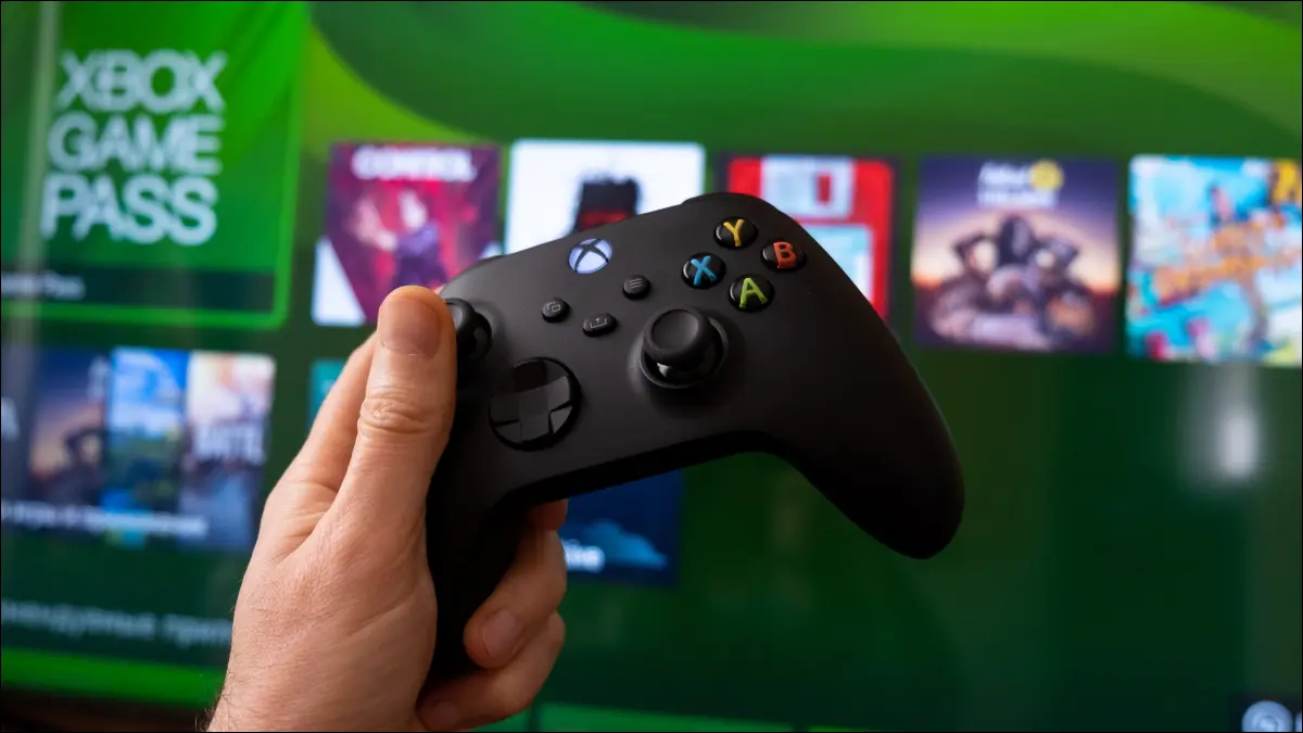 O mână care ține un controler Xbox Series X în fața Game Pass de pe consolă.