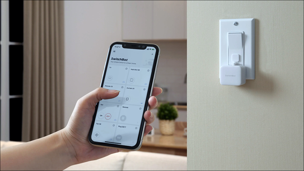 Tenere in mano lo smartphone con l'app SwitchBot in primo piano e SwitchBot Bot in background