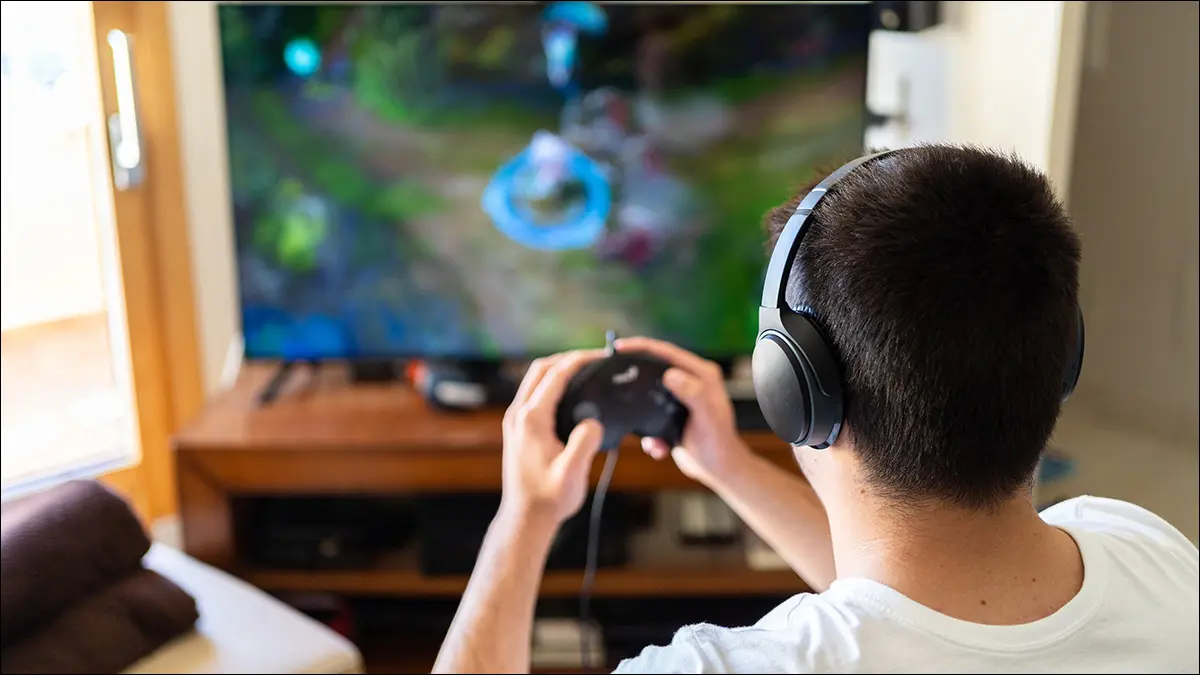 Seseorang bermain video game sambil mengenakan headphone nirkabel.