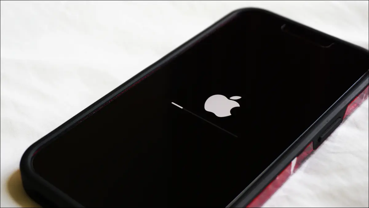 白色桌面上的 iPhone 的特寫鏡頭，屏幕上顯示 Apple 標誌和軟件升級進度條。