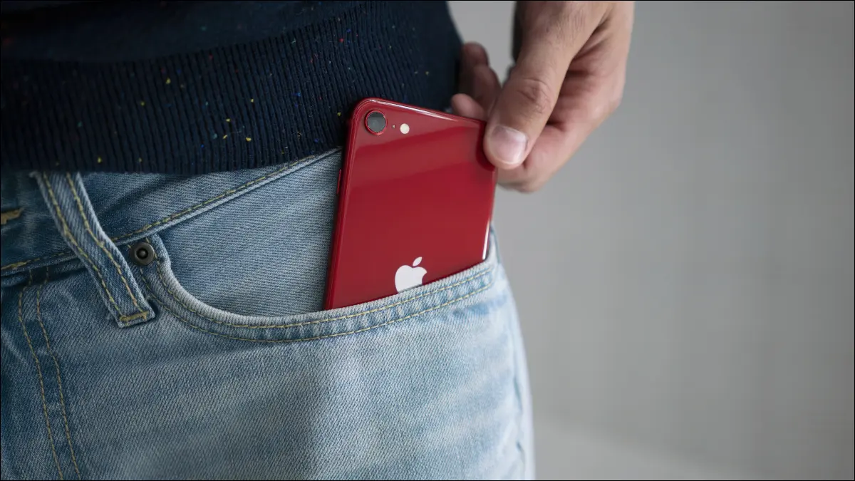 Un iPhone SE rouge (version 2022) sorti de la poche de jean d'une personne.