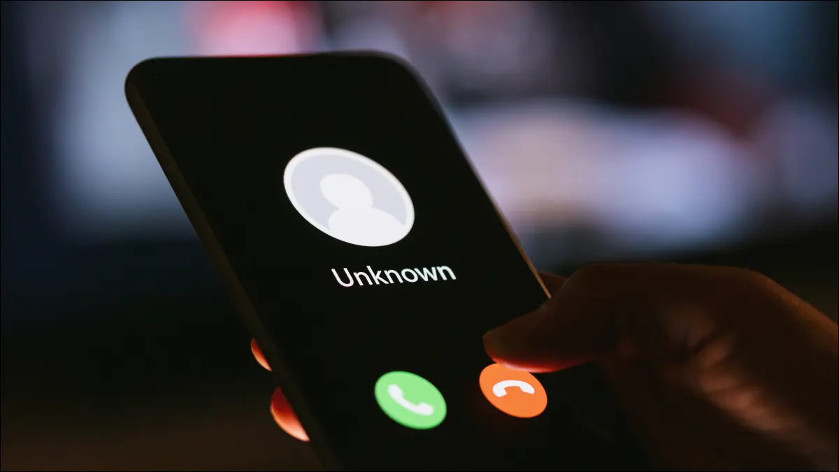 La main d'une personne tenant un smartphone dans l'obscurité, avec un appel d'un appelant inconnu affiché.
