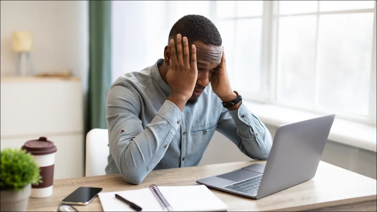 Hombre sentado en el escritorio con una computadora portátil, agarrándose la cabeza con frustración