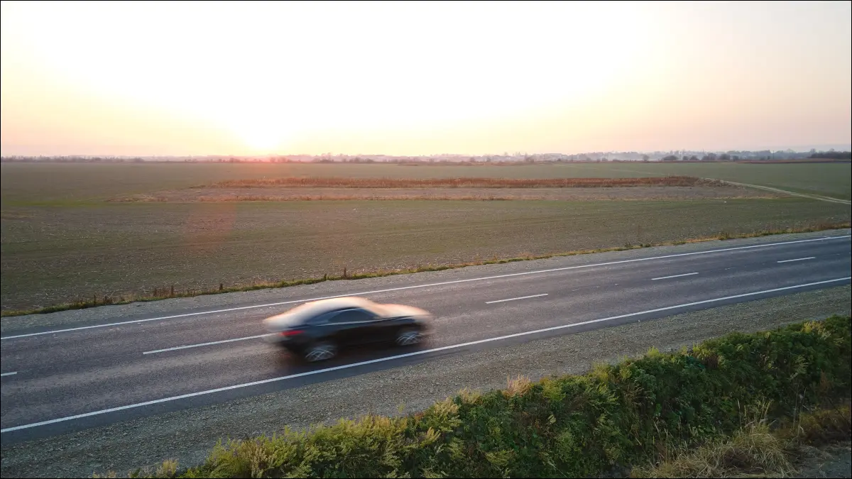 Vista aérea de um veículo elétrico em alta velocidade em um cruzamento de rodovia lança um campo aberto ao pôr do sol.