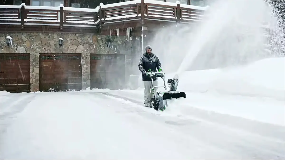 Um homem limpando a entrada de sua garagem com um soprador de neve da marca EGO.