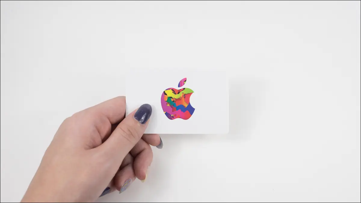 La main de la personne tenant une carte-cadeau Apple sur un fond blanc.