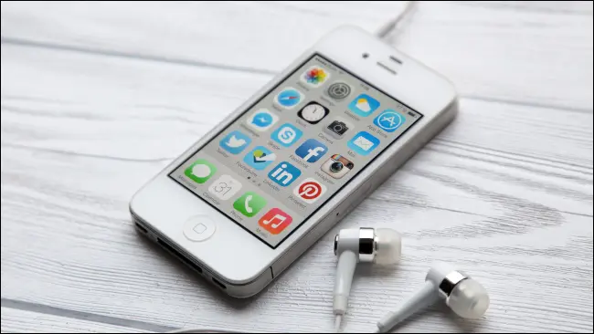 Un iPhone 4 avec écouteurs sur une table en bois blanc.