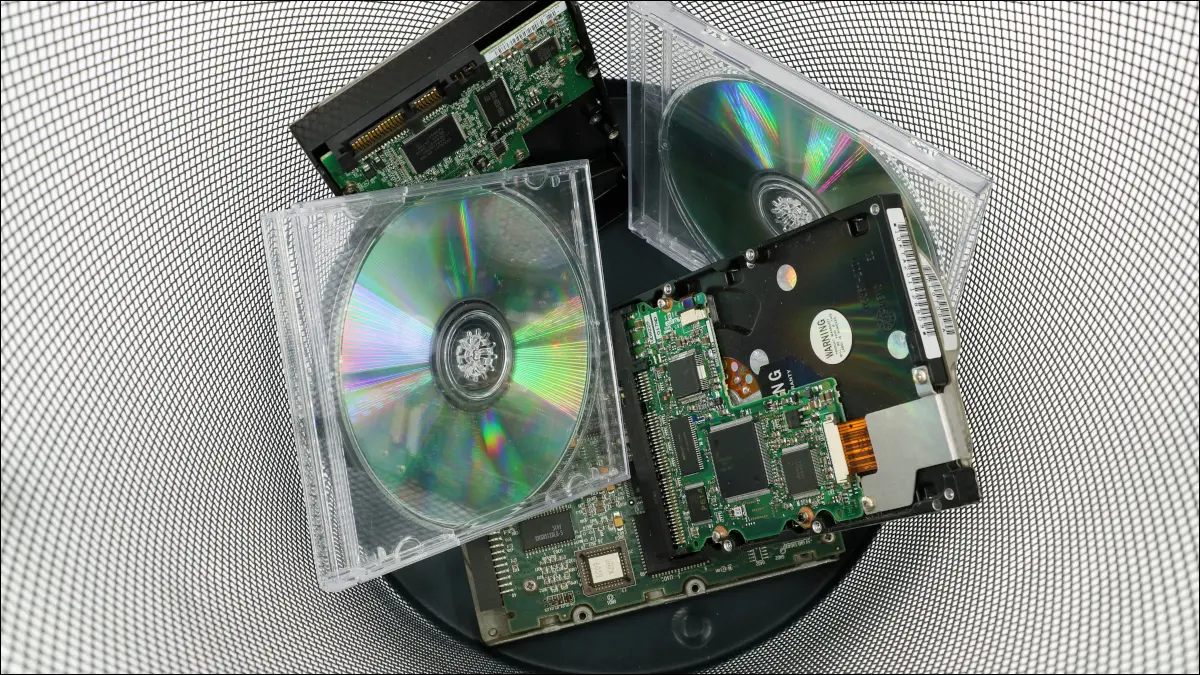 Vecchi compact disc e hardware del computer scartati in un cestino della spazzatura.