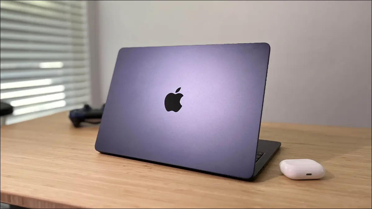 Apple MacBook Air M2 spoczywający na biurku obok słuchawek AirPods Pro i kontrolera PS4