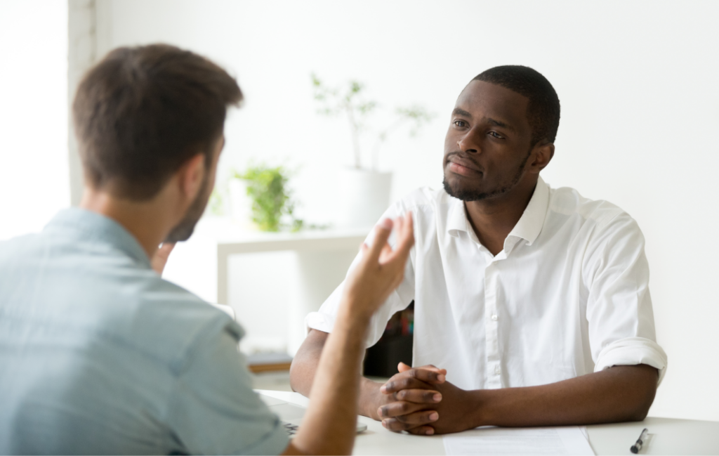 Deux hommes assis à une table discutaient ; l'un écoute attentivement pendant que l'autre parle.